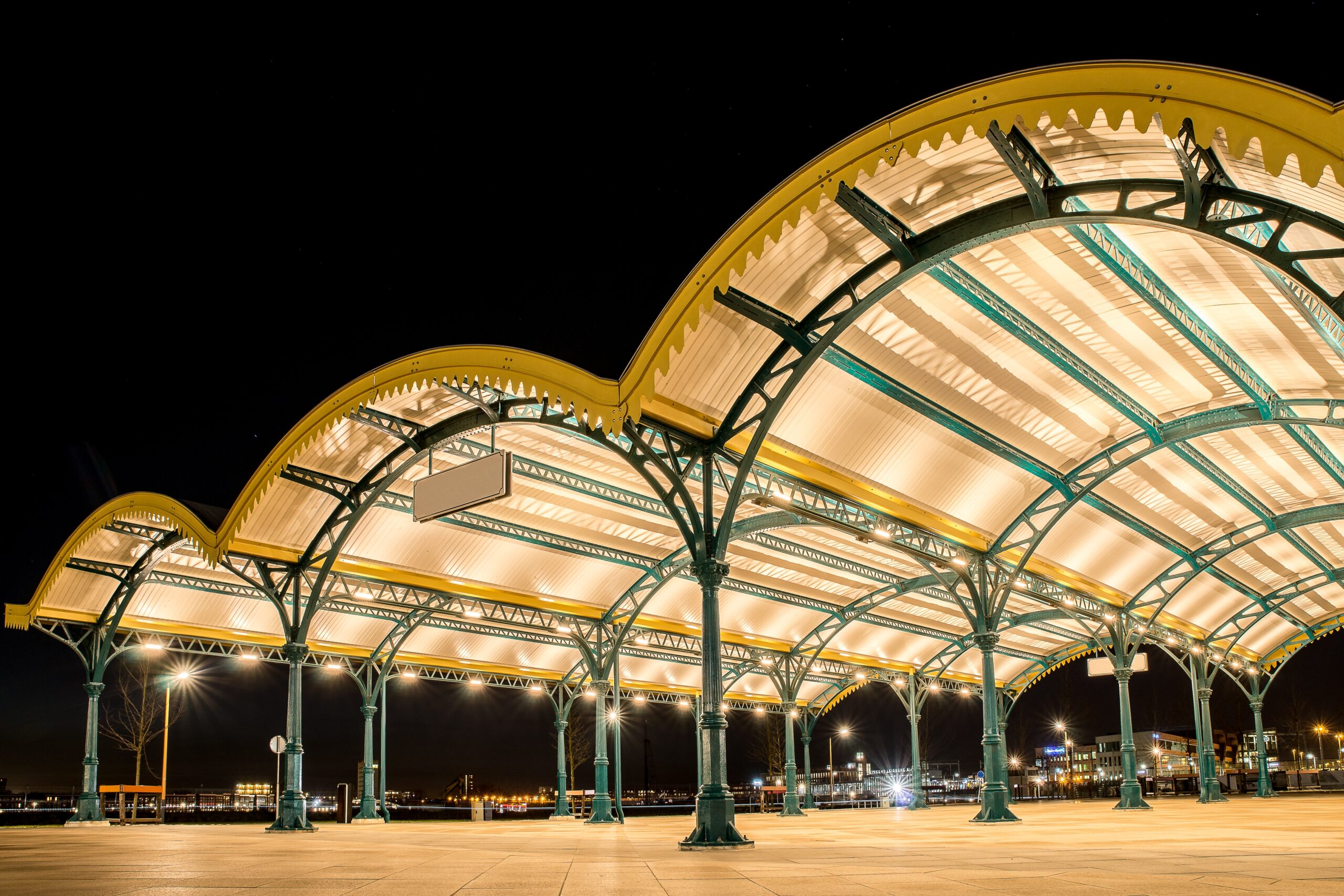 An angled shot of three yellow curved roofs in a city with lights under a dark sky